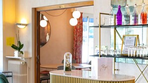 A bar area with two green barstools, a round bar counter, and a shelf with bottles and glasses. - Cit'Hotel Logis de Brou (Bourg-en-Bresse)