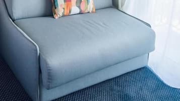 A light grey sofa with a colorful geometric pillow against a teal wall, positioned next to a window with white curtains.