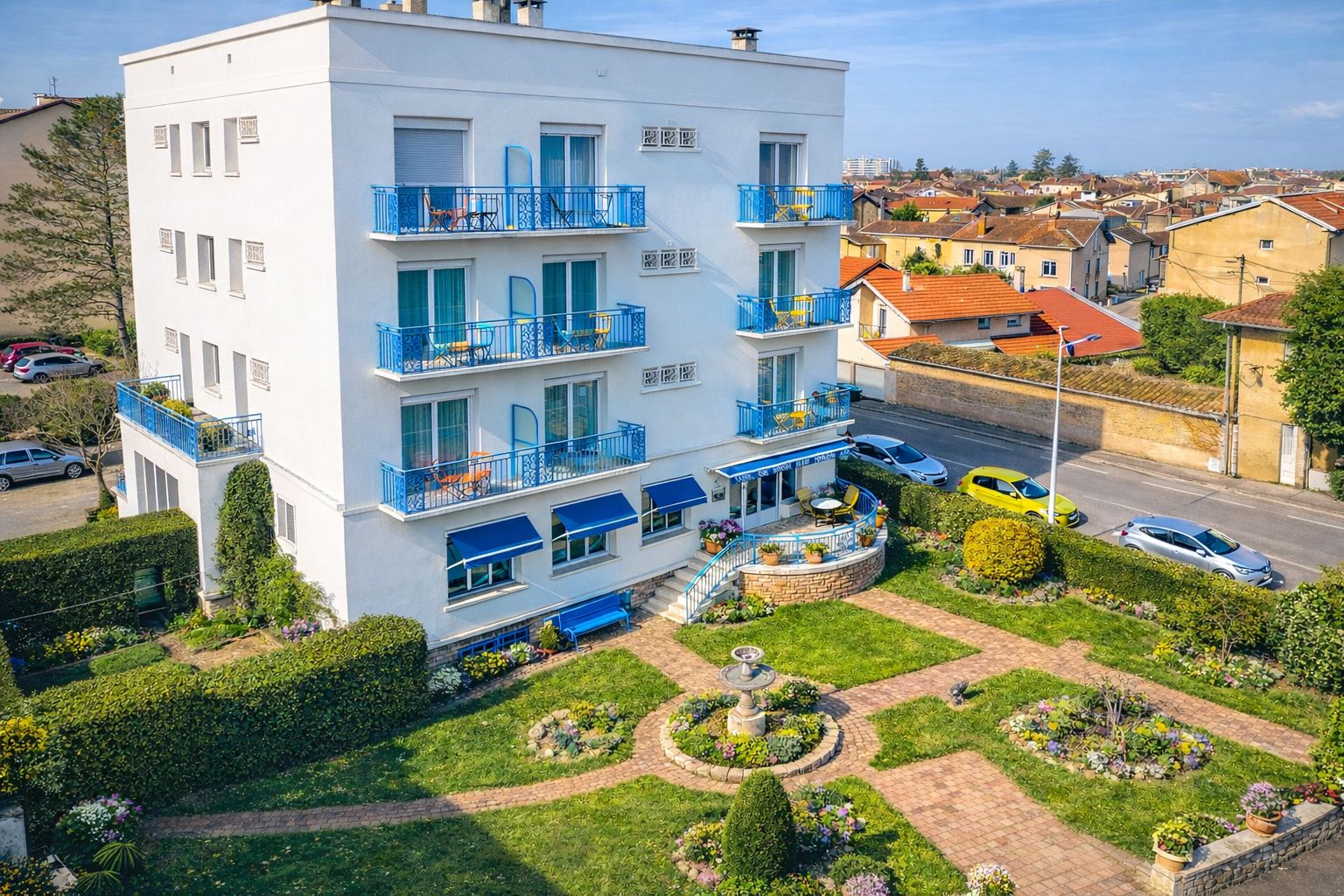 Een hotel met meerdere verdiepingen, balkons, een tuin met zonnewijzer en een parkeerplaats.