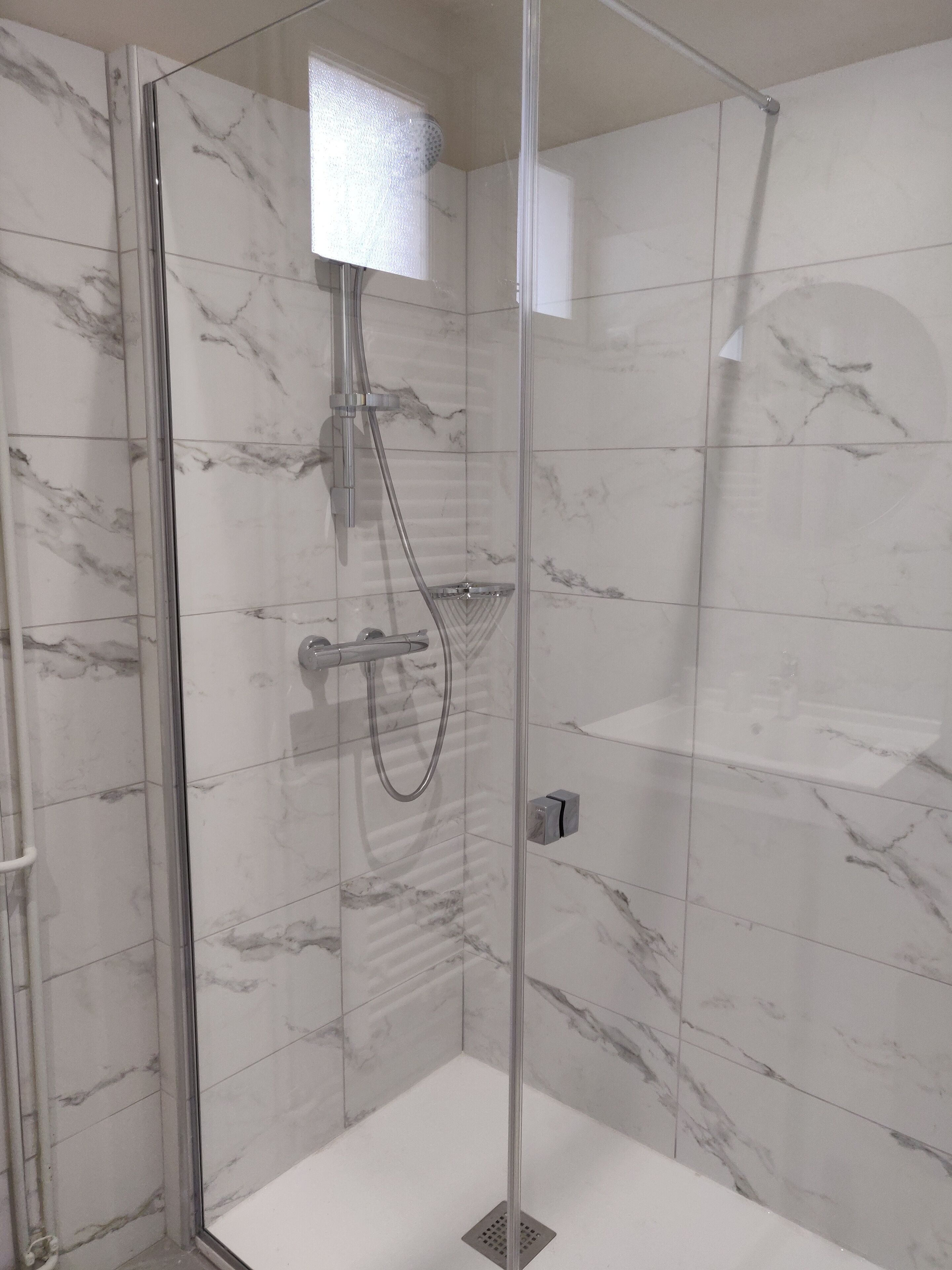 Une douche fermée par des parois en verre, dotée d’un pommeau de douche à main et d’un flexible de douche à main.