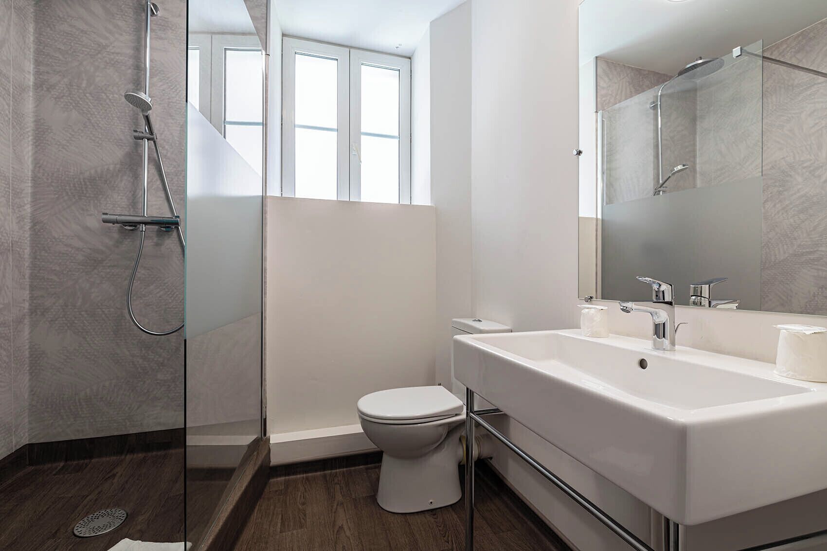 Een moderne badkamer met een glazen douchecabine, een wit toilet en een grote spiegel boven een witte wastafel.