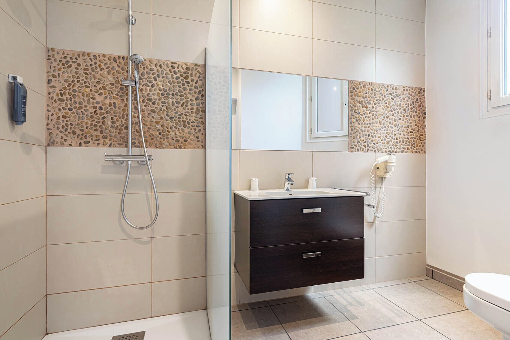 Un baño moderno con ducha, tocador con espejo y retrete.