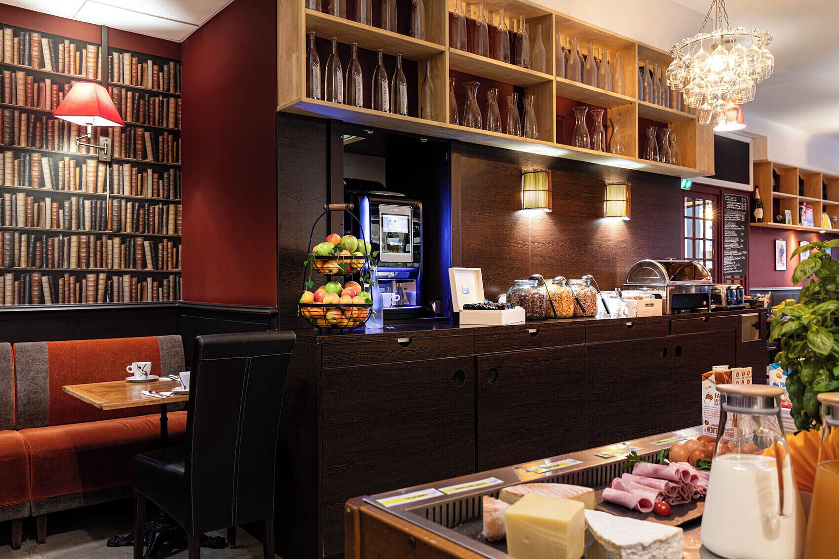 A cozy cafe with bookshelves, a coffee machine, and a variety of food items displayed on the counter.