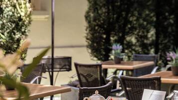 An outdoor cafe with wicker chairs and tables, a tea set, and a book.