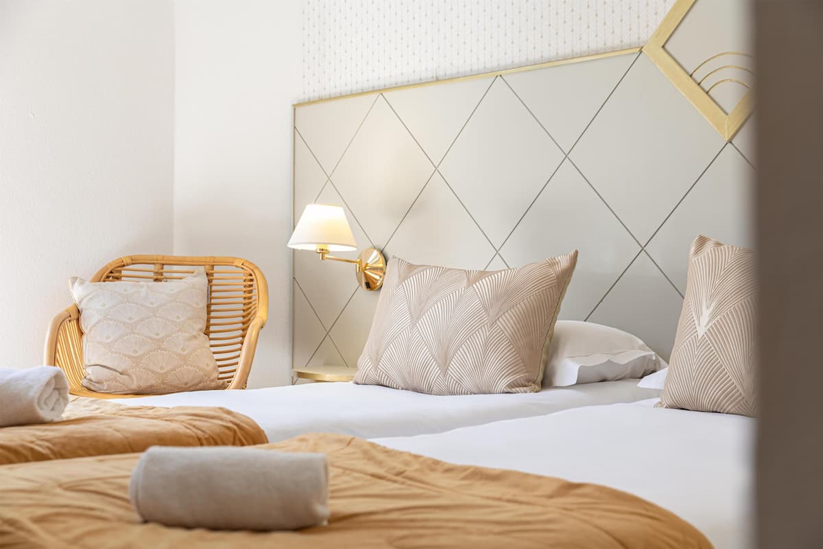 Habitació d'hotel amb un llit, una cadira i una tauleta de nit amb una làmpada.