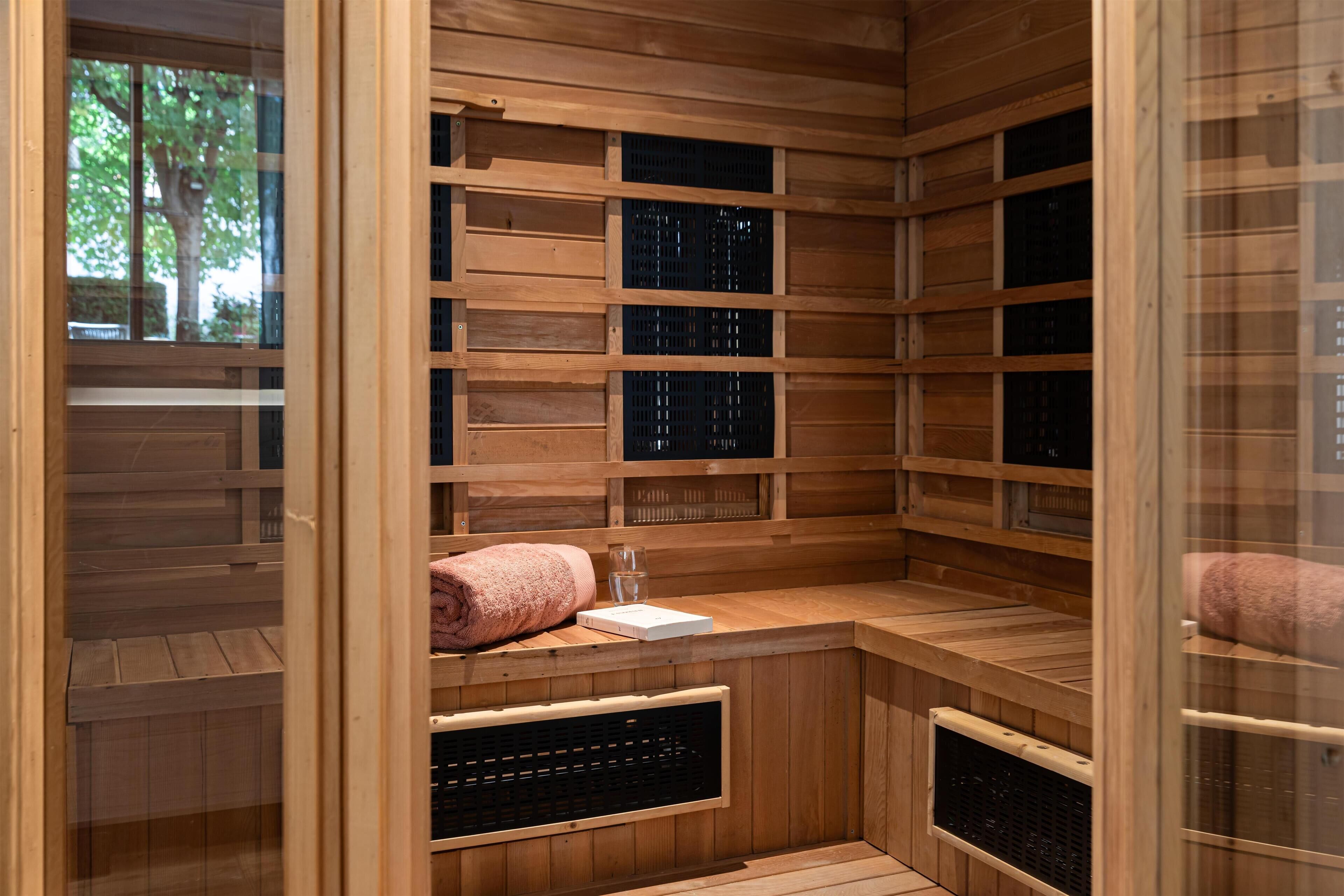 Una sauna con paredes y bancos de madera, una puerta de cristal y una toalla sobre uno de los bancos.