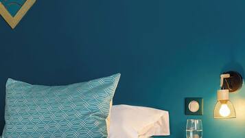 A neatly made bed with a teal headboard and a patterned pillow, a bedside table with a lamp, and a framed picture on the wall.