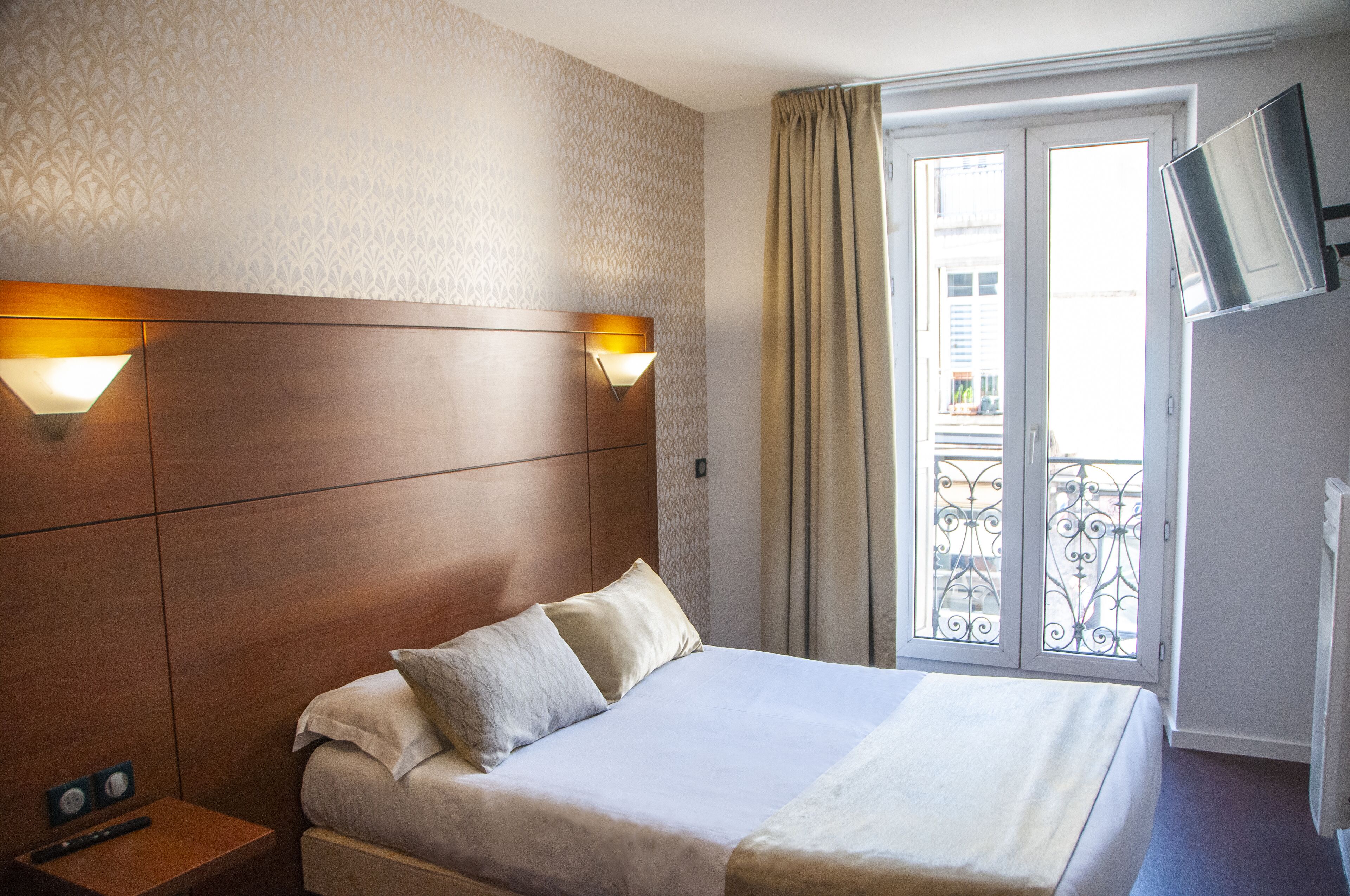 A hotel room with a bed, two bedside lamps, a TV, and a window with curtains.