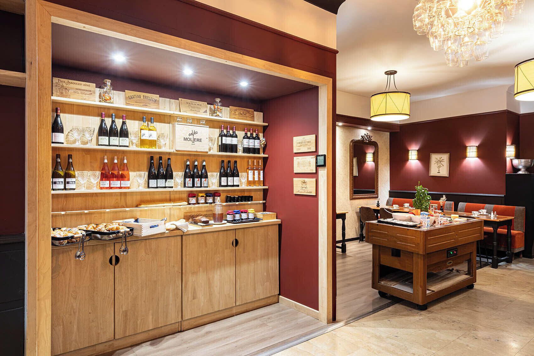 A wine cellar with wooden shelves displaying various wine bottles and glasses, a wooden counter with pastries, and a dining area with a table and chairs.