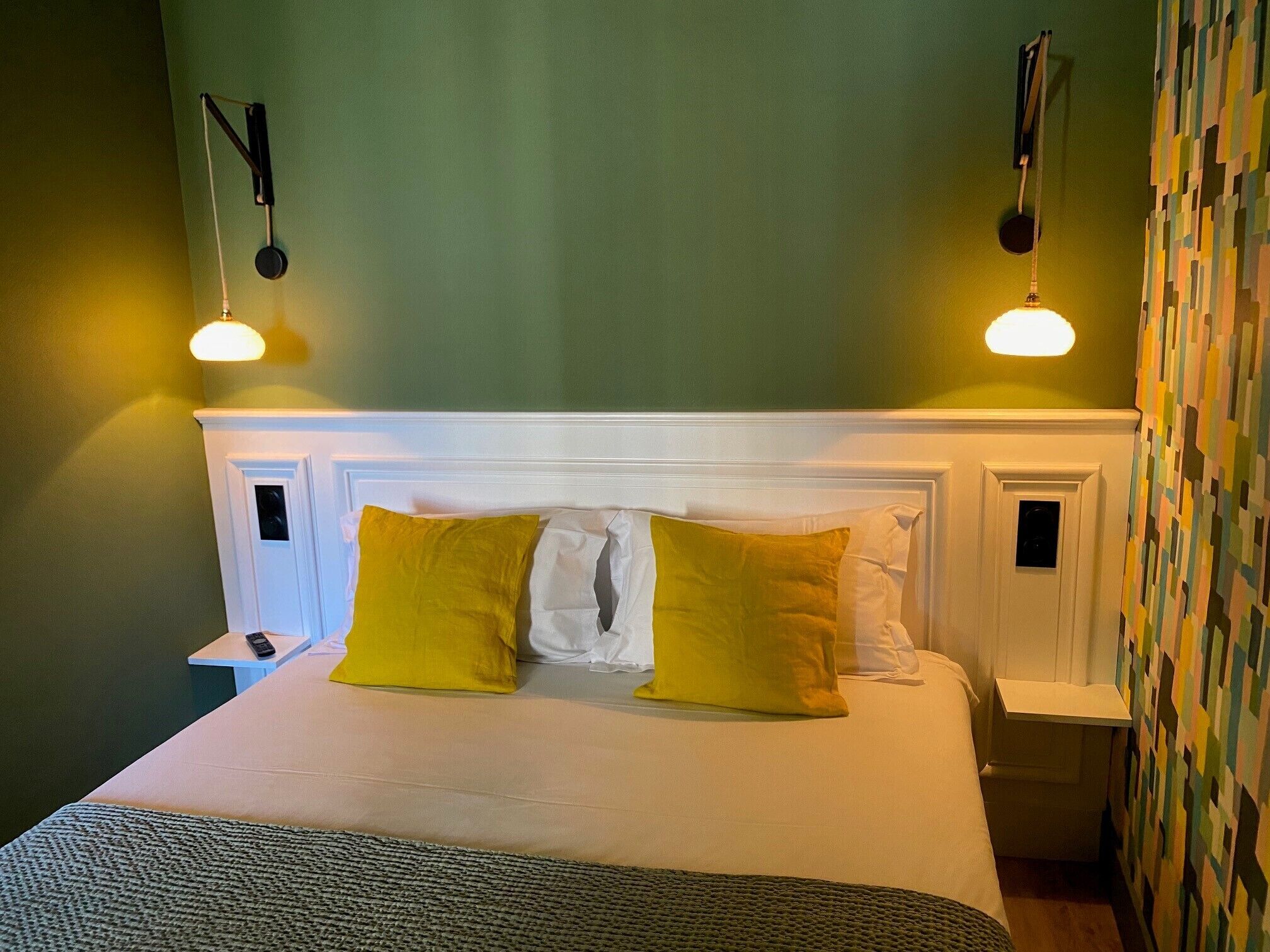 A neatly made bed with white and yellow pillows, a white headboard, and two bedside tables with lamps.