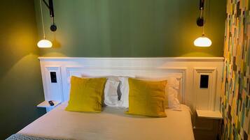 A neatly made bed with white and yellow pillows, a white headboard, and two bedside tables with lamps.
