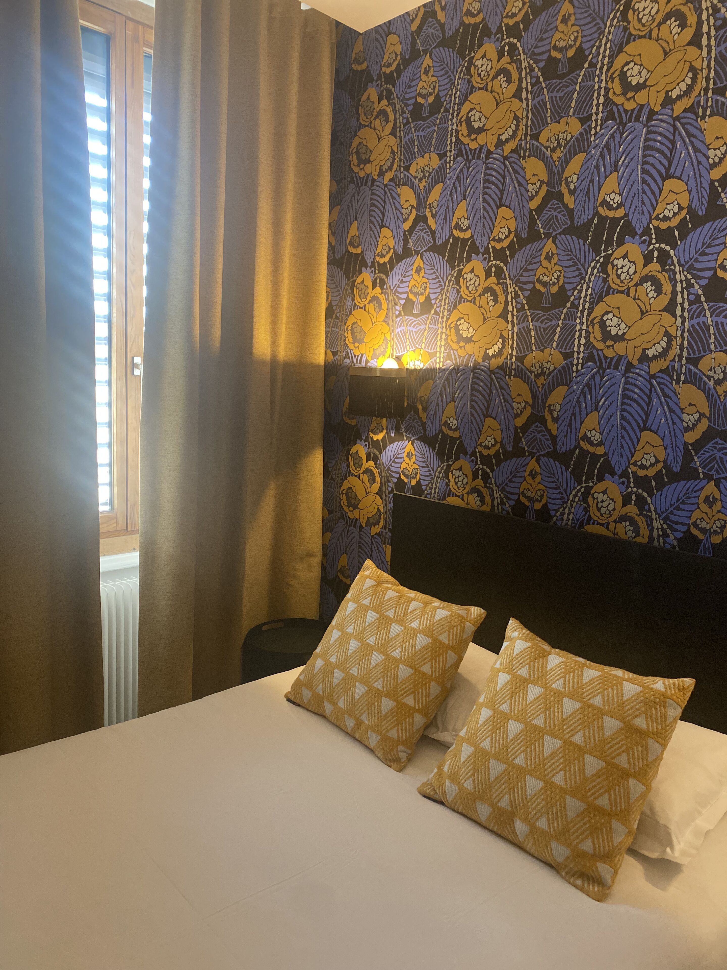 Hotelkamer met een bed, twee gestreepte kussens, een nachtkastje, een lamp en een raam met gordijnen.