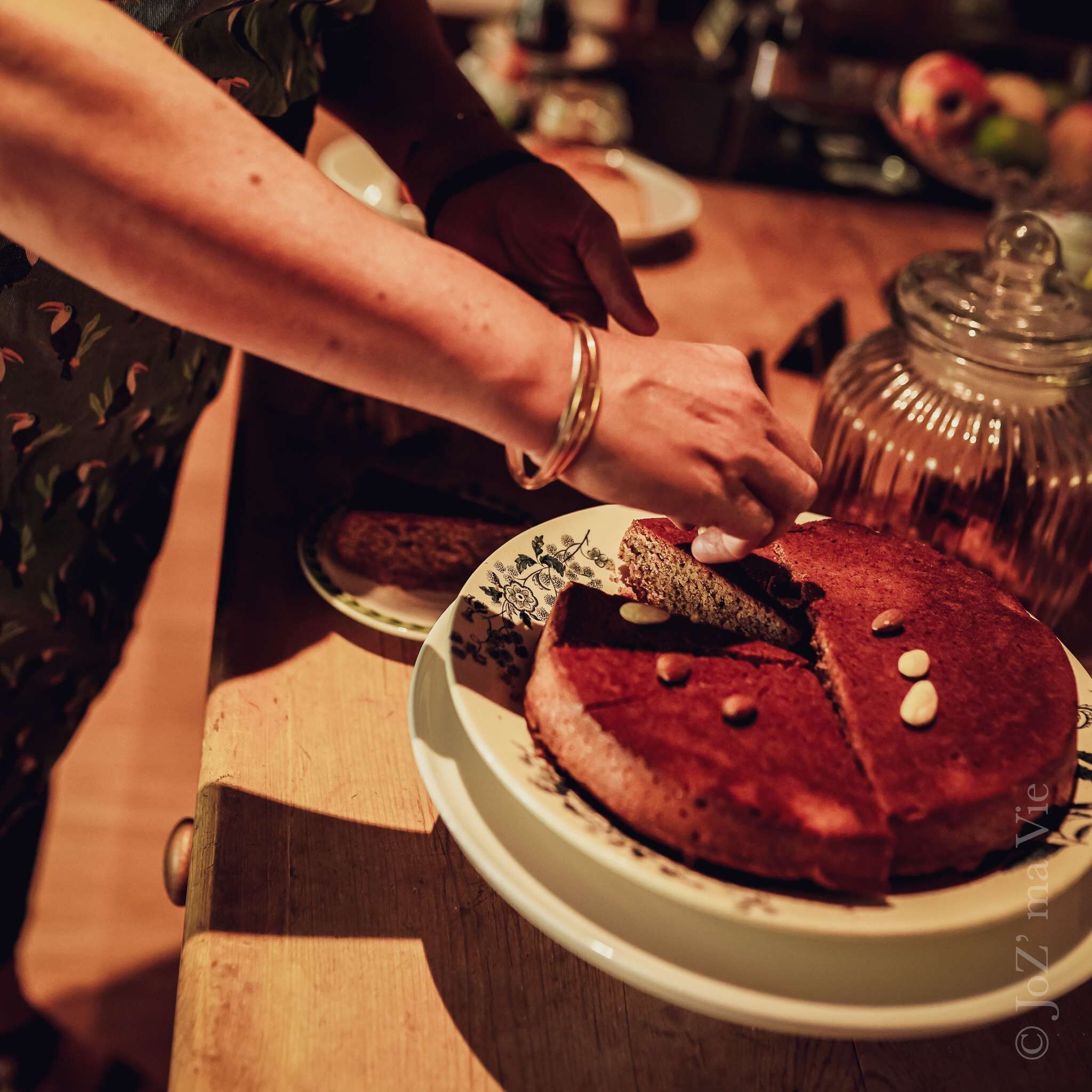 A person cutting a cake on a wooden table with a glass jar in the background.