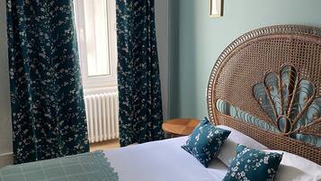 A bedroom with a bed, floral curtains, a rattan headboard, and a small wooden side table.
