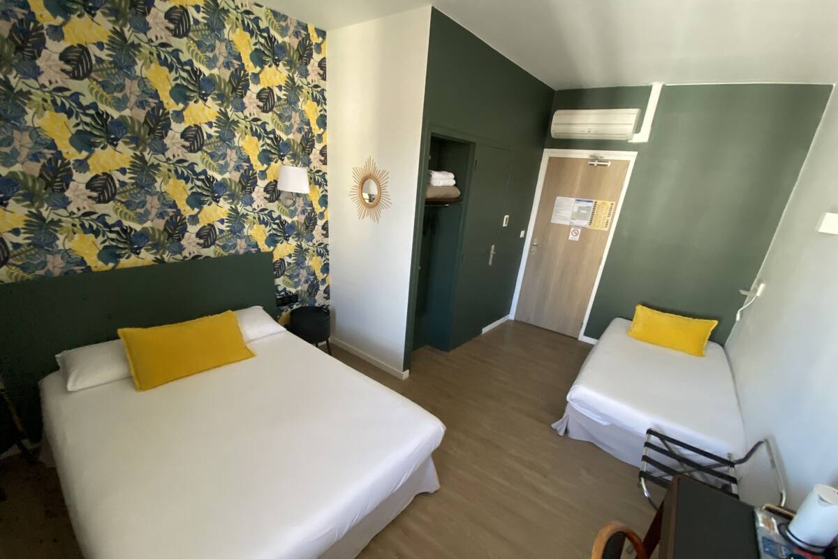 A hotel room with two beds, a mirror, a wall-mounted air conditioner, and a wooden floor.