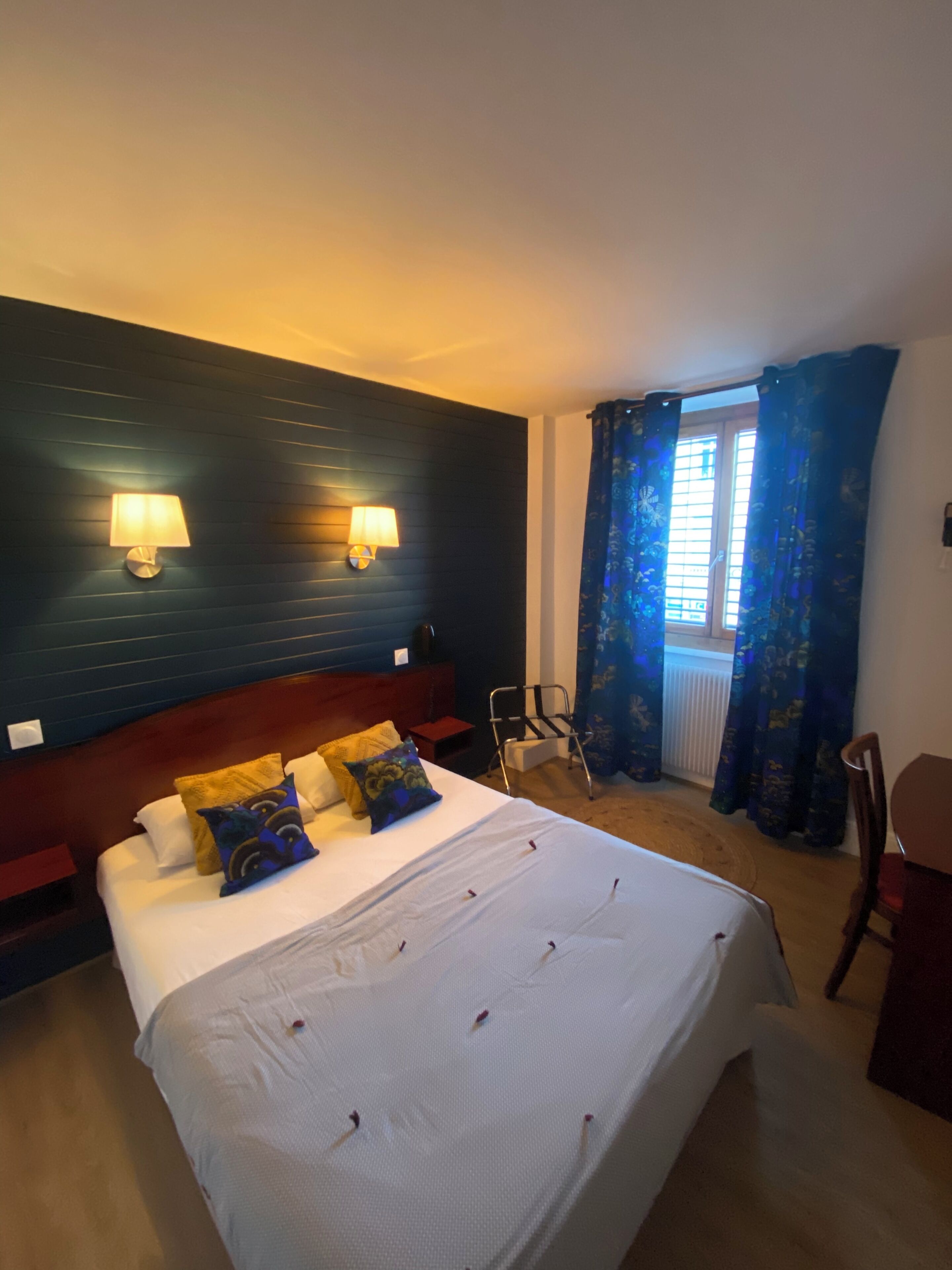 Ein Hotelzimmer mit einem großen Bett, zwei Wandleuchten, einem Fenster mit blauen Vorhängen und einem Sessel.