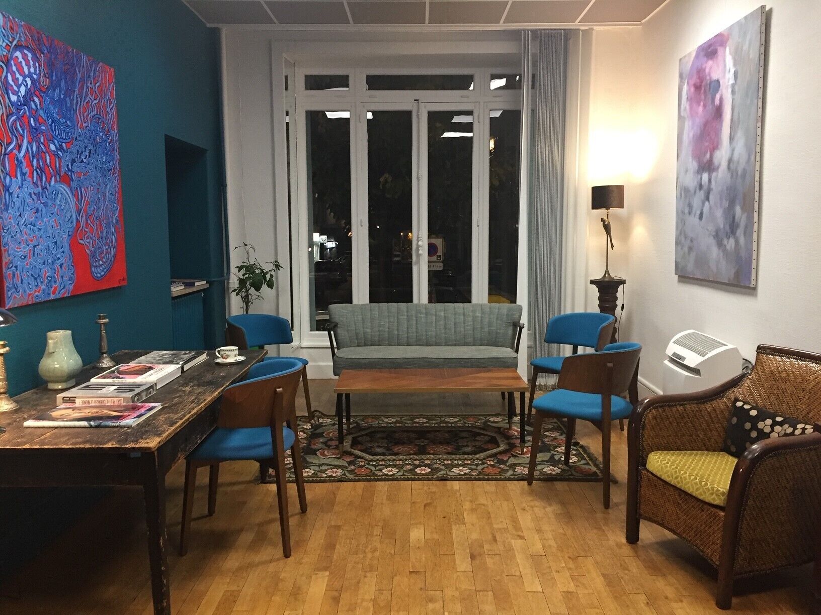 A cozy living room with a sofa, chairs, a coffee table, and a dining table with books and a lamp.