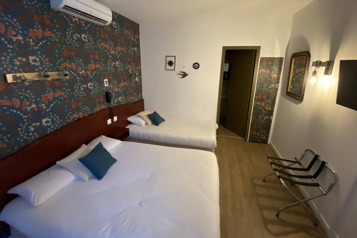 A hotel room with two beds, a wooden headboard, a wall-mounted air conditioner, a mirror, and a chair.
