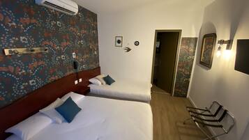 Ett hotellrum med två sängar, en sänggavel i trä, en väggmonterad luftkonditioneringsanläggning, en spegel och en stol.