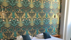 A hotel room with a large bed, two bedside tables, and a wall with a floral wallpaper pattern. - Grand Hotel de la Poste (Vienne)
