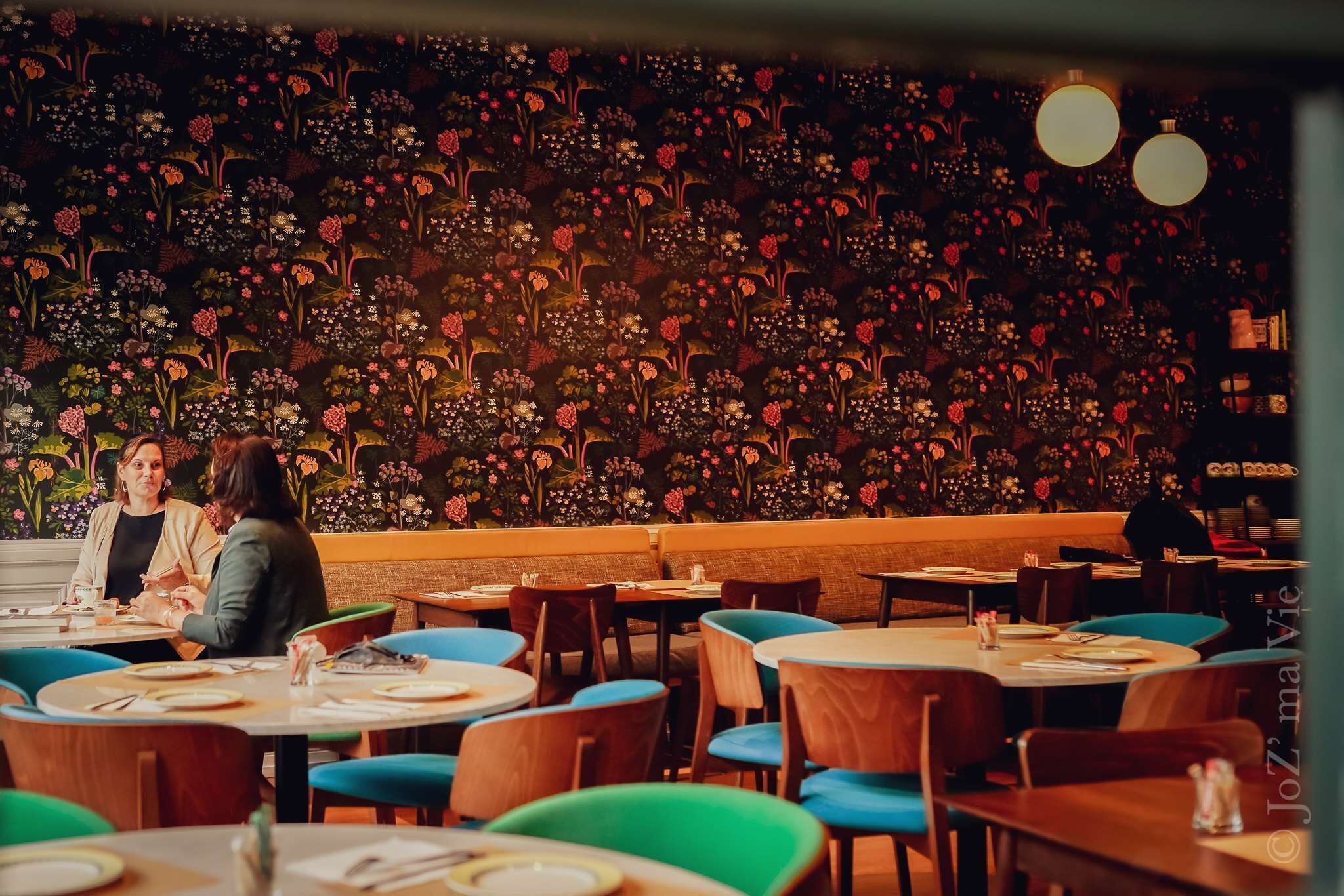 A restaurant with round tables and chairs, a floral wall mural, and hanging lights.