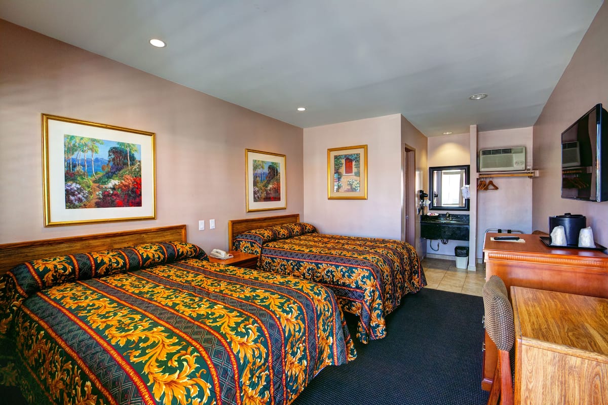 A hotel room with two beds, a desk, a chair, a TV, and framed pictures on the walls.