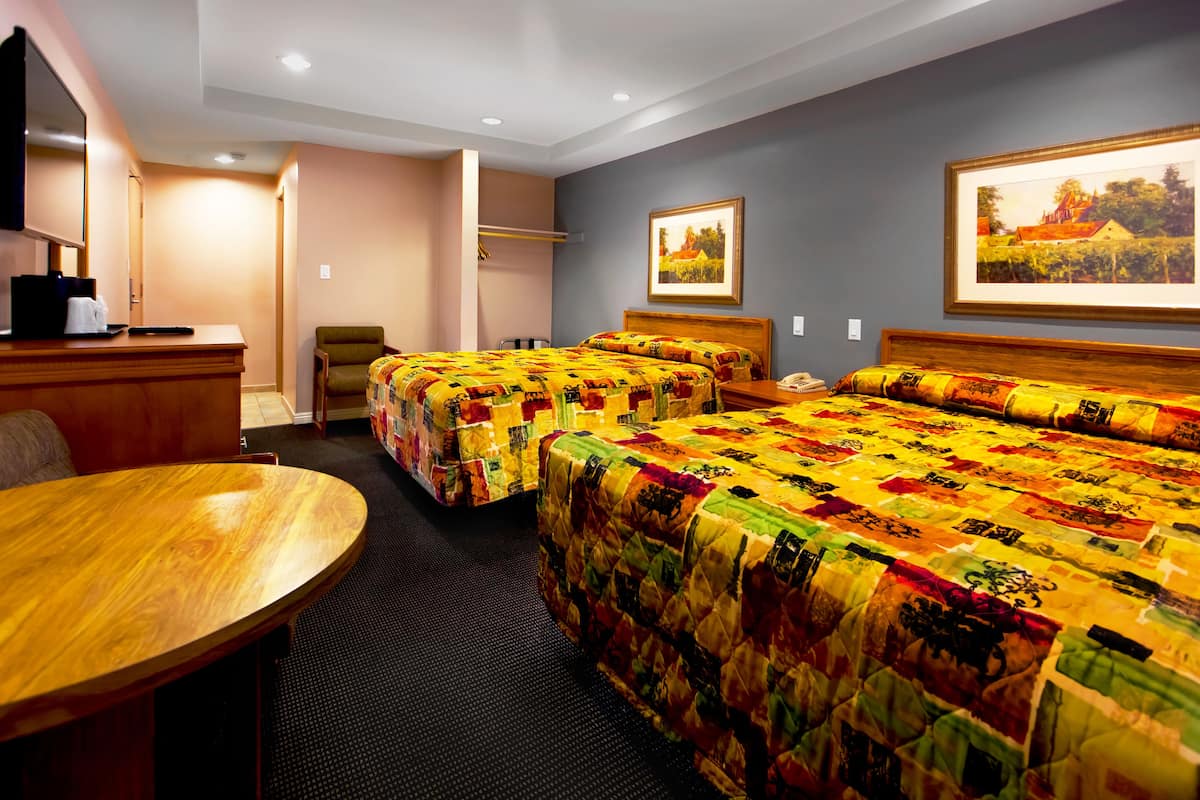 A hotel room with two beds, a desk, a chair, and a dining table.