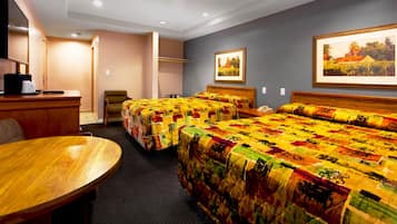 A hotel room with two beds, a desk, a chair, and a dining table.