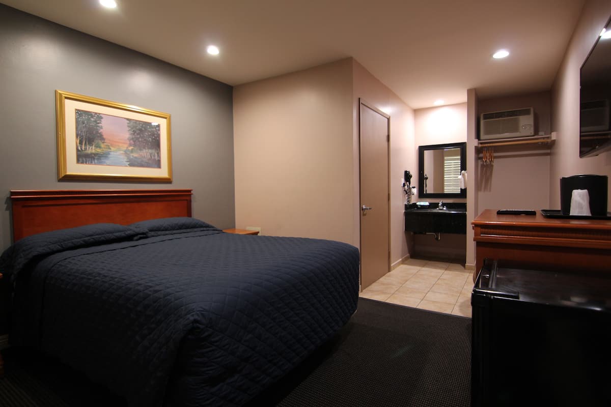 A hotel room with a bed, a painting on the wall, a bathroom with a mirror, and a desk with a coffee maker.