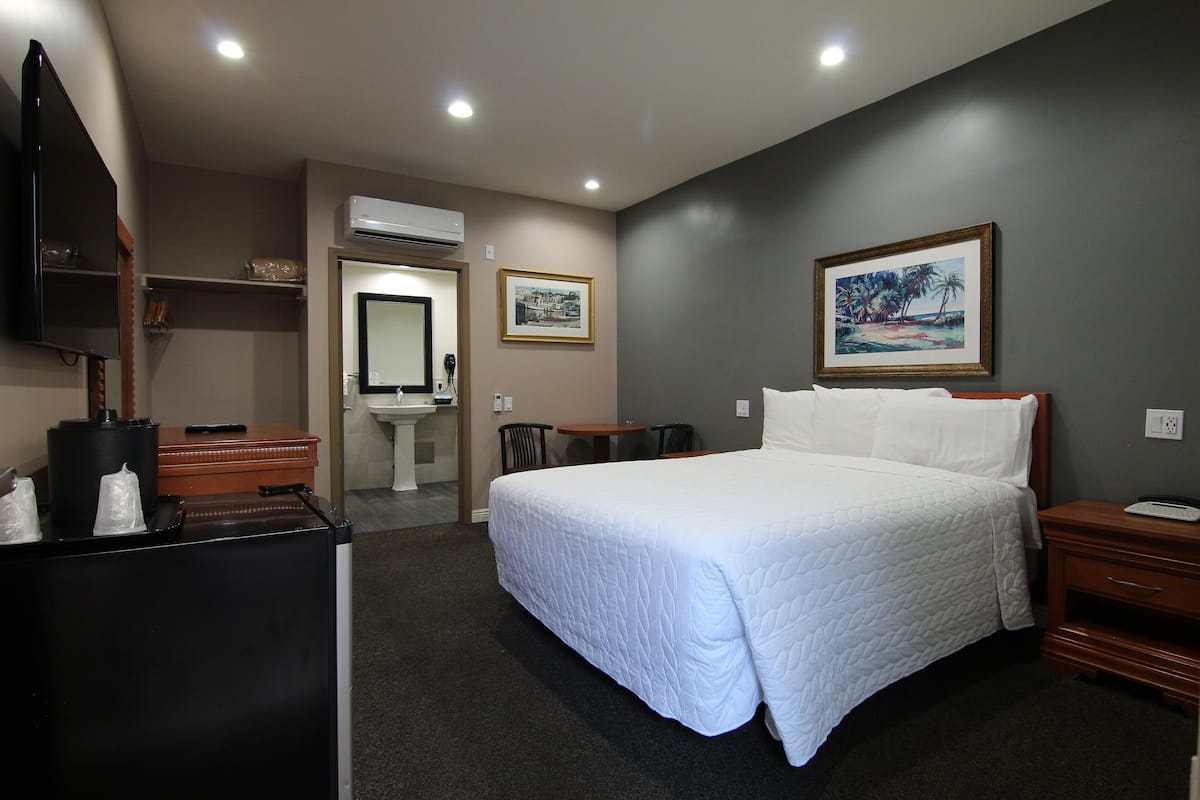 A hotel room with a large bed, a desk with a computer, a chair, a small table, and a wall-mounted TV.