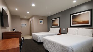 A hotel room with two beds, a desk, a flat-screen TV, and framed pictures on the walls.