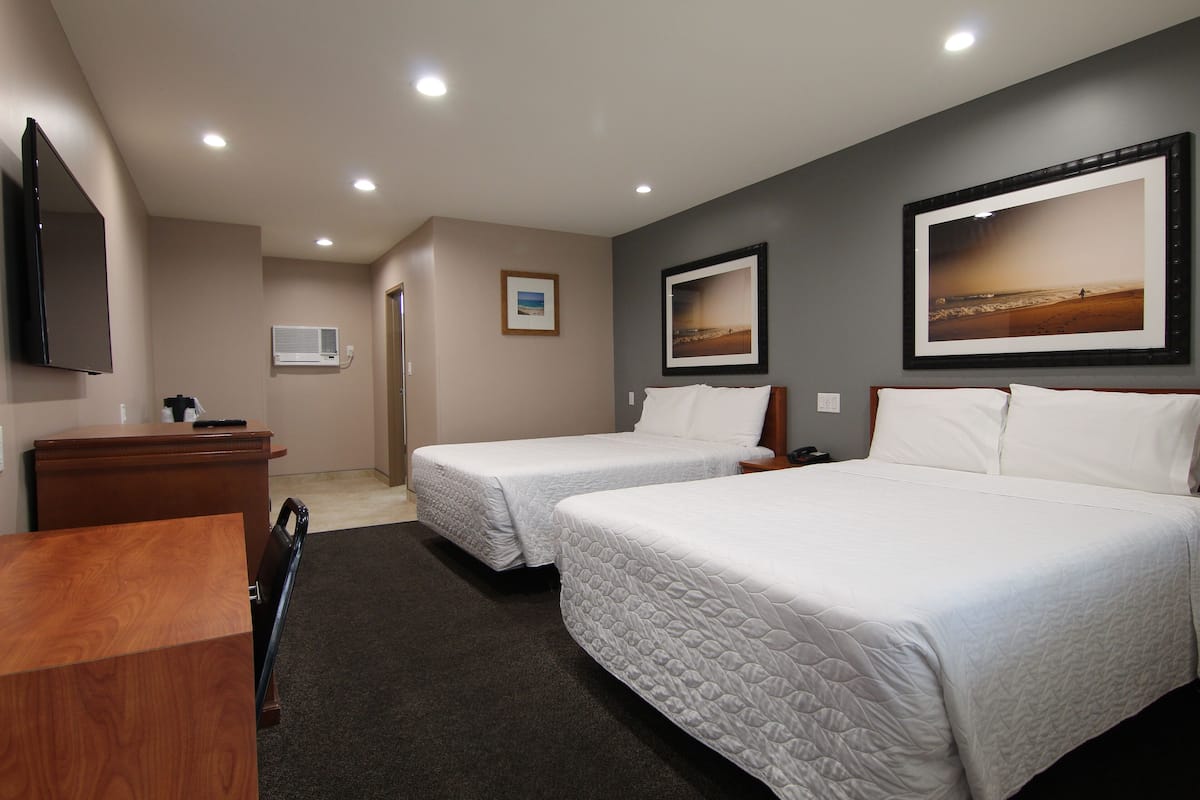 A hotel room with two beds, a desk, a flat-screen TV, and framed pictures on the walls.