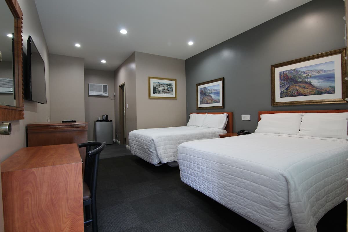A hotel room with two single beds, a wooden desk, a chair, a TV, and framed pictures on the walls.