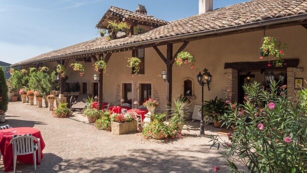 Un edificio con techo de tejas, mesas al aire libre y cestas de flores colgantes.