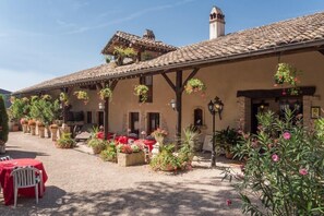 A building with a tiled roof, outdoor seating, and hanging flower baskets. - Hostellerie Sarrasine (Replonges)