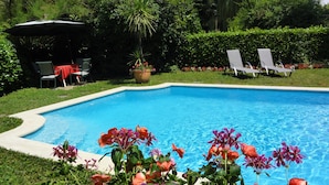 Una piscina rodeada de abundante vegetación y un jardín con diversas plantas y flores.