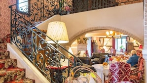 Una majestuosa escalera con barandillas de metal decorativas lleva a un comedor con sillas rojas de estampado y una mesa preparada para una comida.