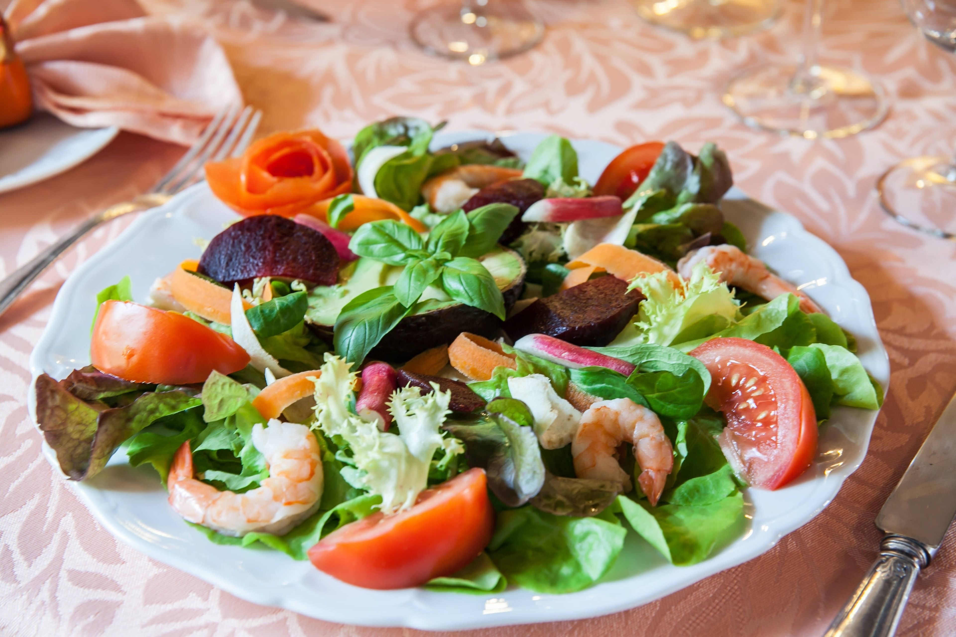 A plate of mixed greens and vegetables with shrimp and tomato slices.