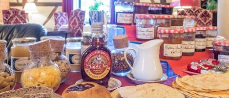 A table with various food items including bread, jars of preserves, and maple syrup.