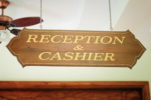 A wooden sign with the words "RECEPTION & CASHIER" hanging from a ceiling.
