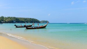 A beach with clear turquoise water and a sandy shore. There are traditional long-tail boats moored near the water's edge. - Bangtao Village Resort (Choeng Thale)