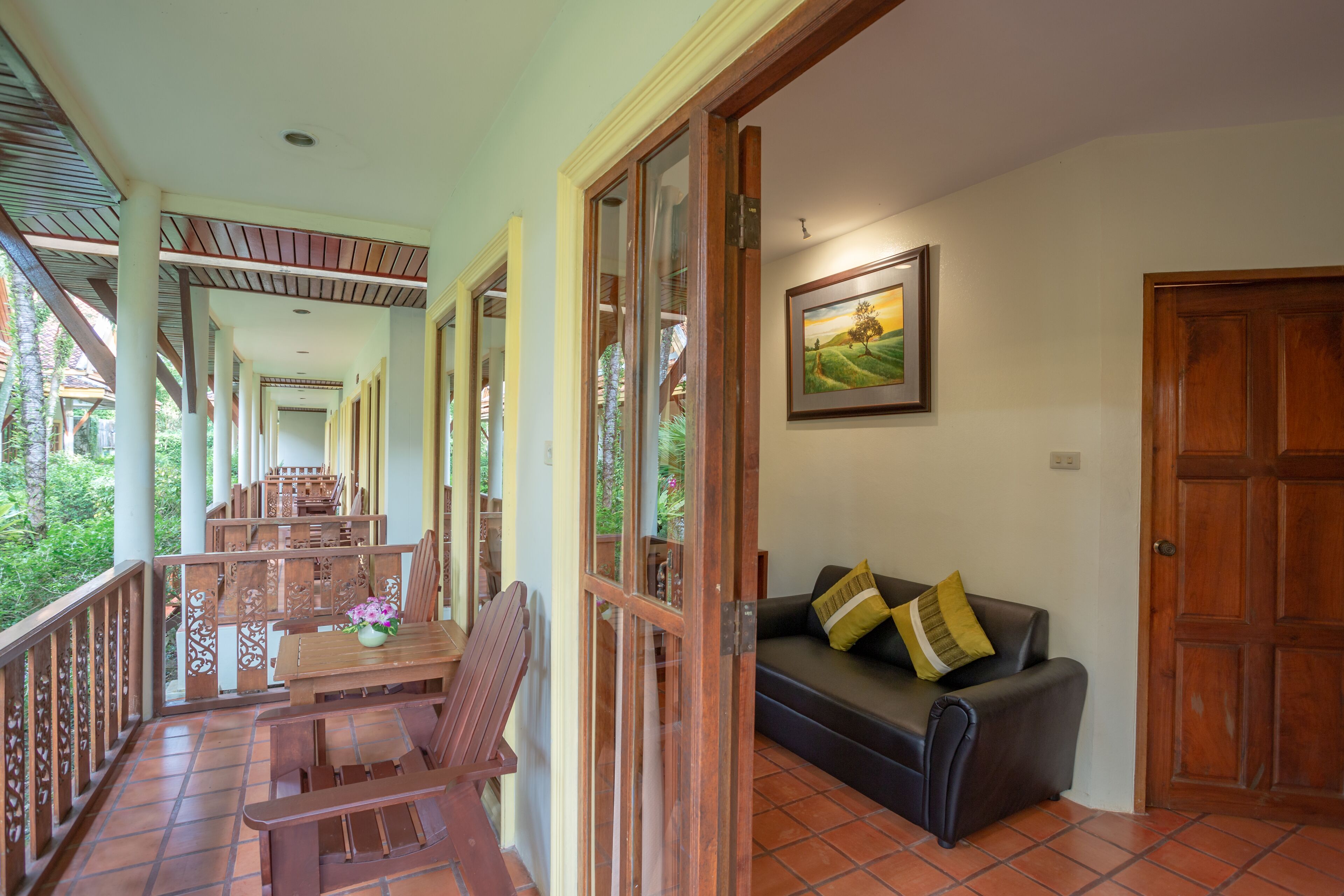 A spacious balcony with wooden furniture, a sofa with cushions, and a framed landscape painting on the wall.