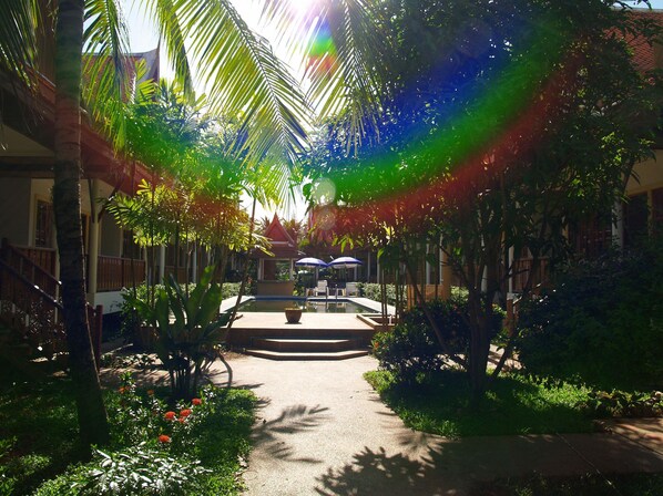 A courtyard with a central pool, surrounded by palm trees and a traditional building with a tiled roof.
