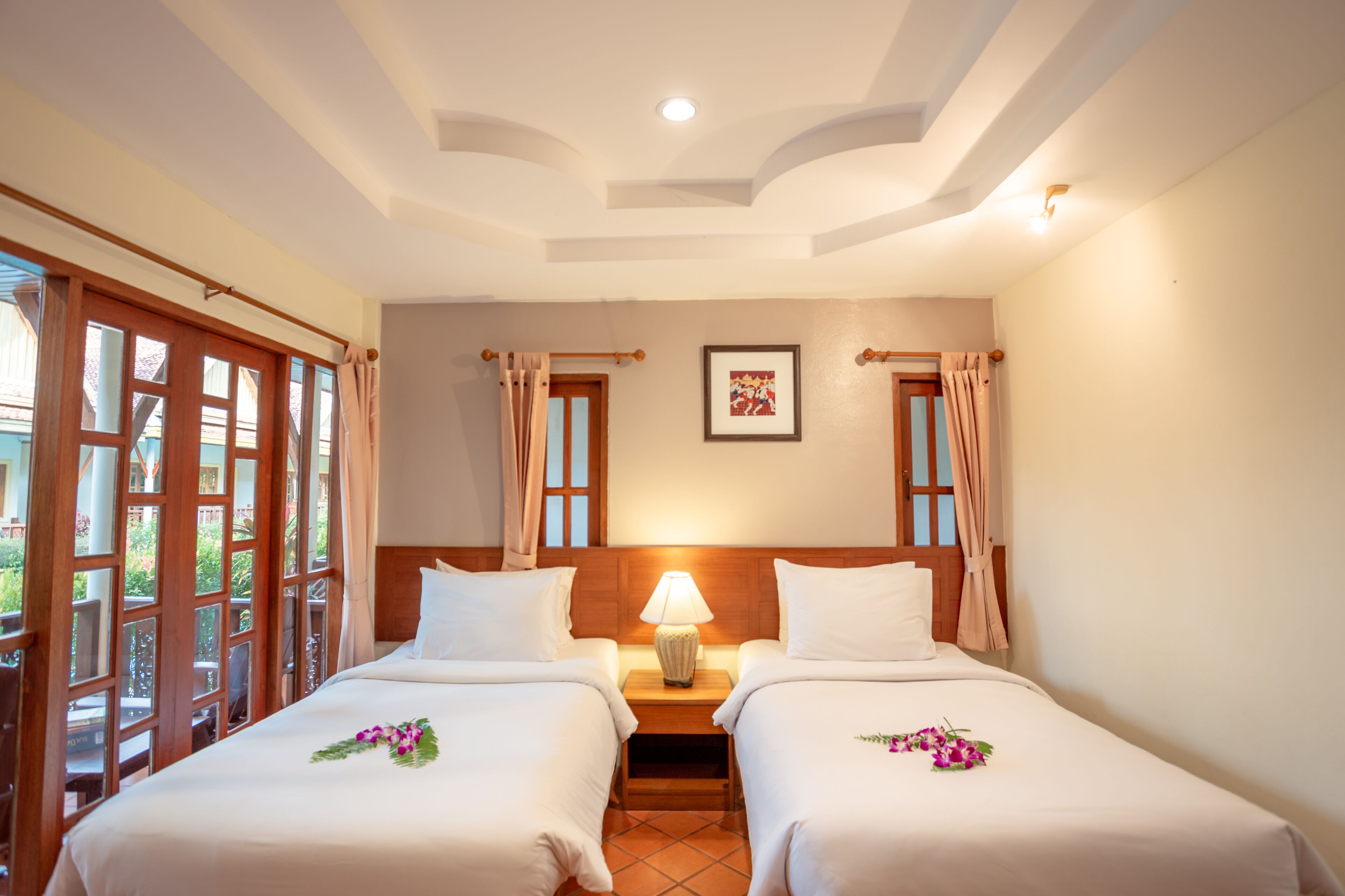 A hotel room with two beds, a nightstand with a lamp, a framed picture on the wall, and a window with curtains.