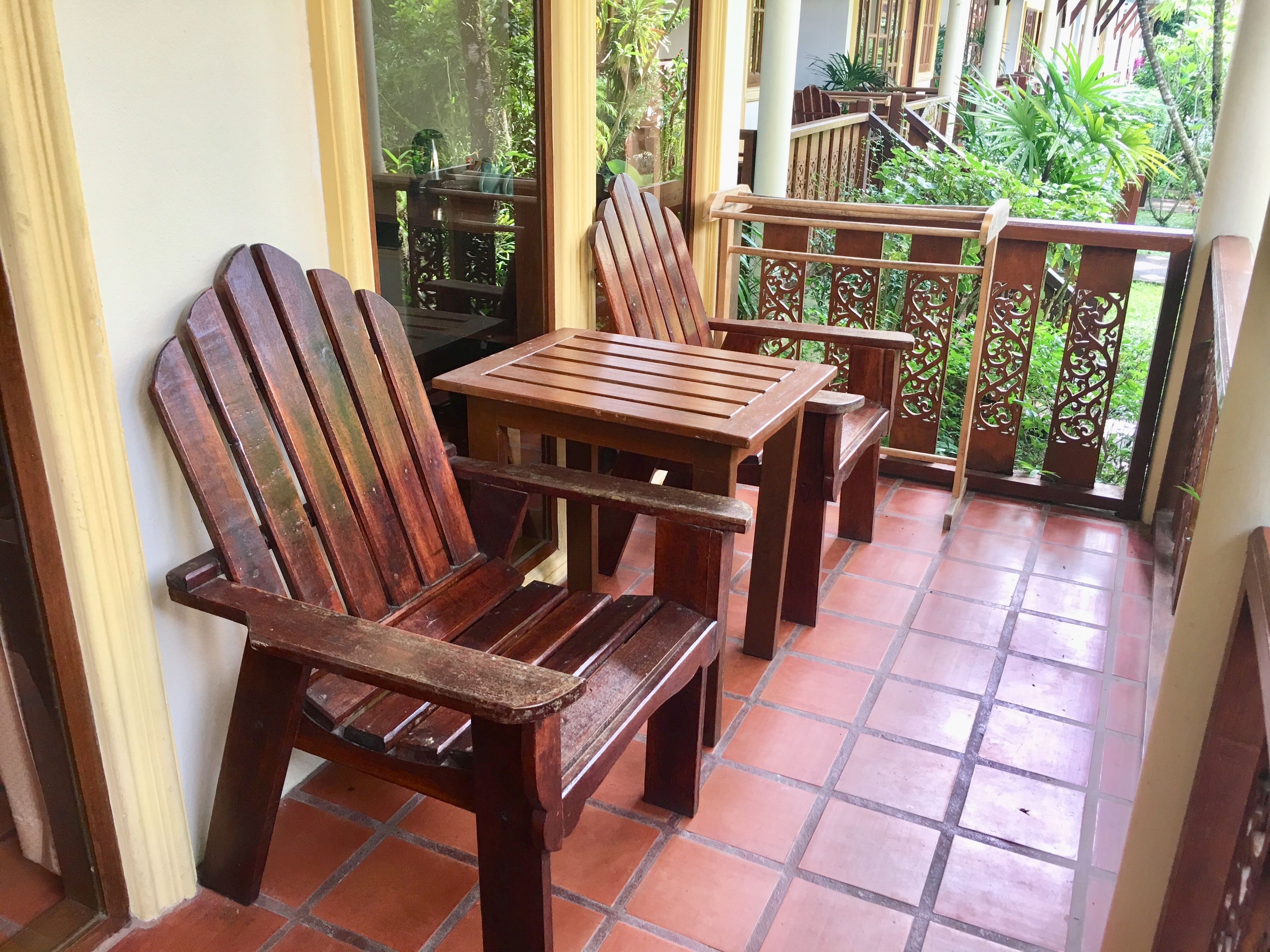 A wooden bench and table set on a tiled patio with a view of greenery.