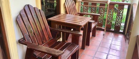 A wooden bench and table set on a tiled patio with a view of greenery.
