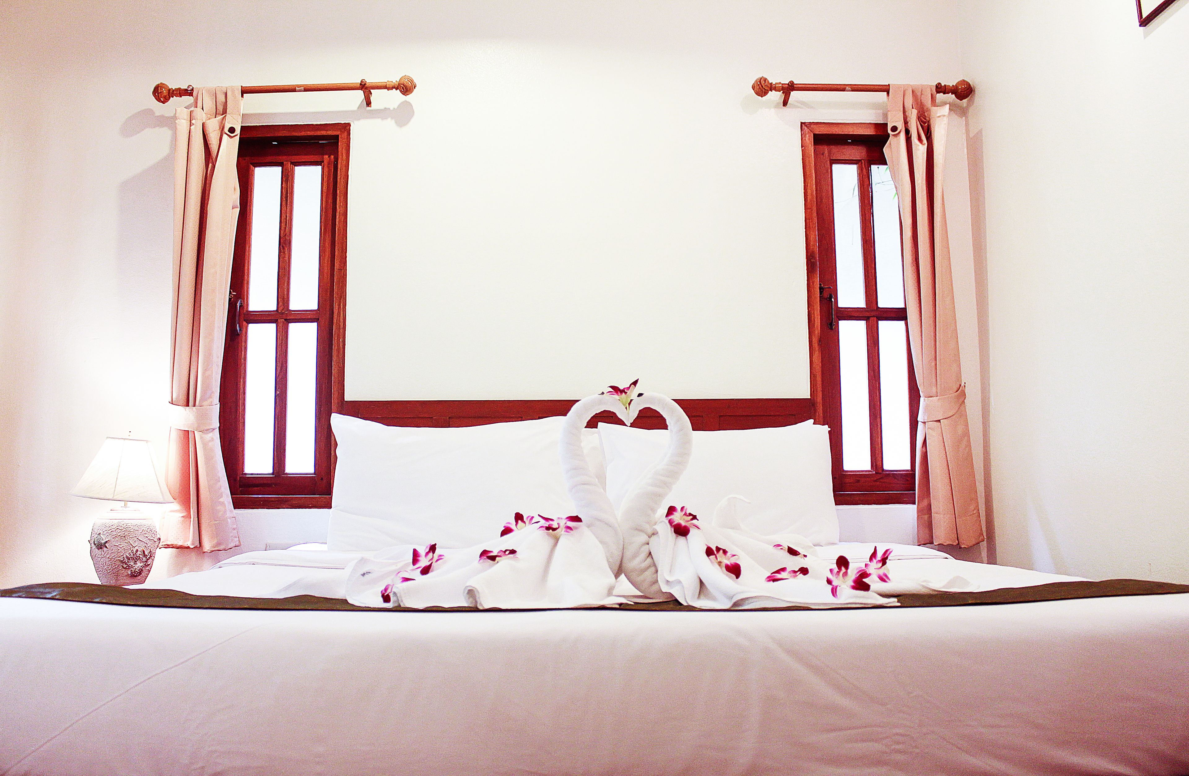 Une chambre d’hôtel avec un lit, des rideaux, une fenêtre et une table de chevet avec une lampe.