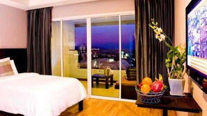 Una habitación de hotel con cama, puerta corrediza de vidrio a un balcón, una mesita con fruta y un televisor en la pared.