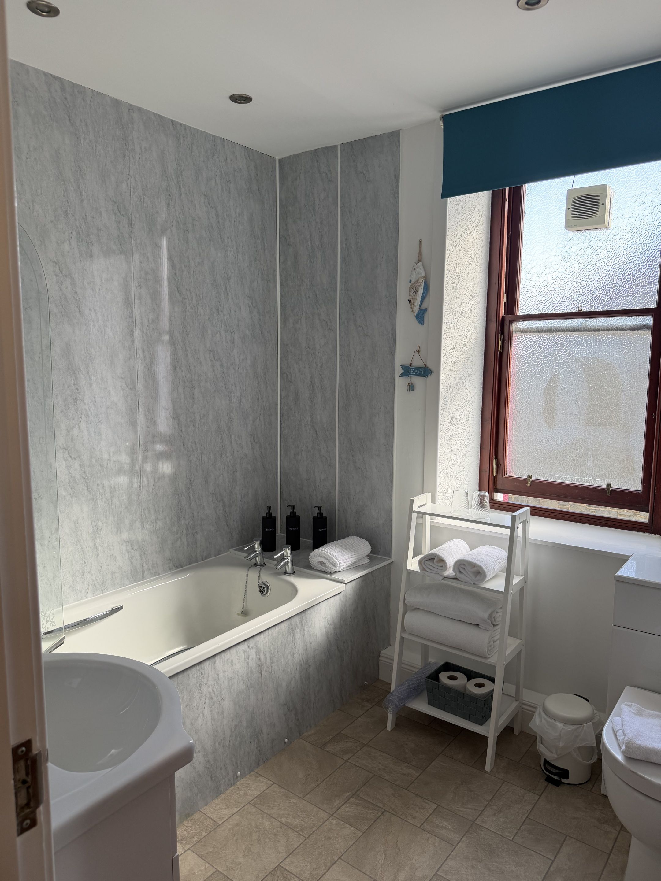 Un baño con bañera, inodoro, lavamanos y toallero, además de un ventanal.