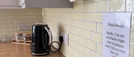 A kitchen with a kettle, a sign, and a tiled backsplash.